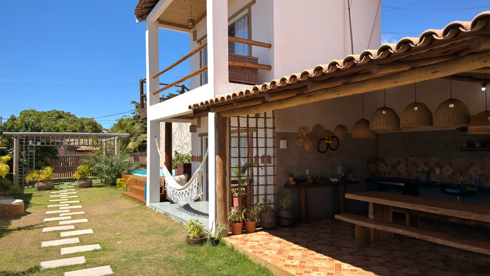 Fachada da casa com varanda, rede e jardim com caminho de pedras
