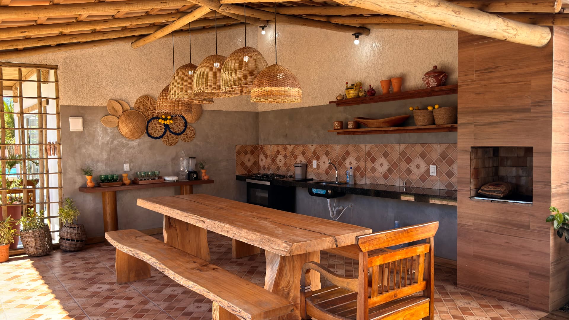 Cozinha gourmet externa com mesa de madeira e luminárias de palha